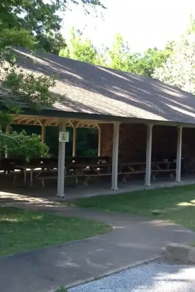 Pavilion with picnic tables, surrounded by trees and grass.