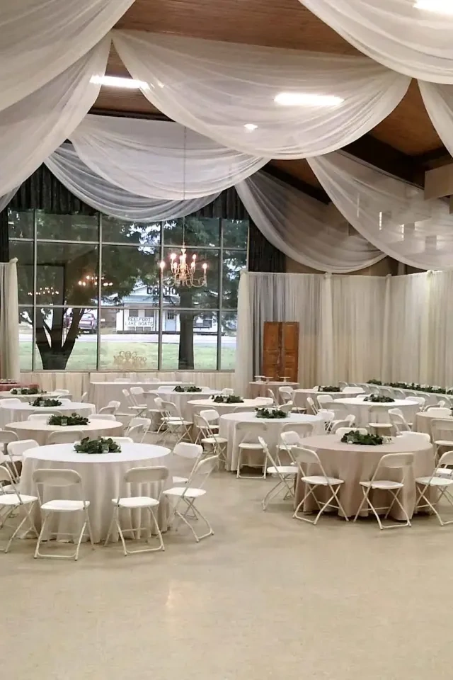 Elegant hall with round tables, white chairs, and draped ceilings.