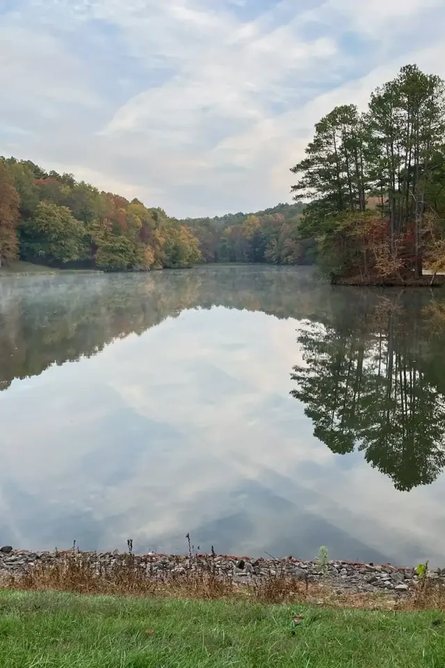 Calm lake with autumn trees reflecting on the water, grassy foreground.