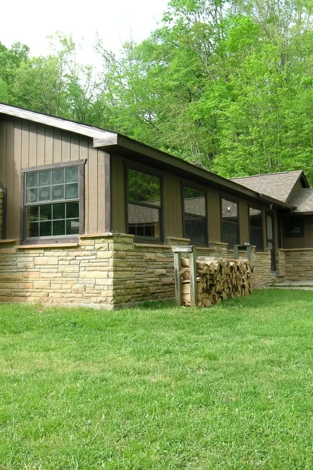 Rustic cabin with stone chimney surrounded by green lawn and trees.