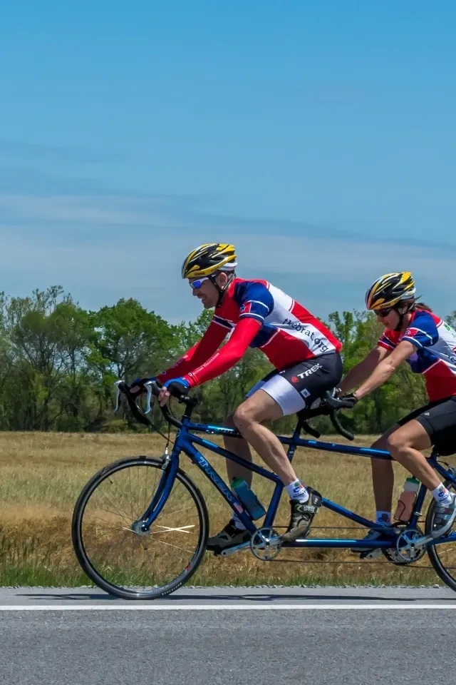Two cyclists on a tandem bike in a rural area under a clear blue sky.