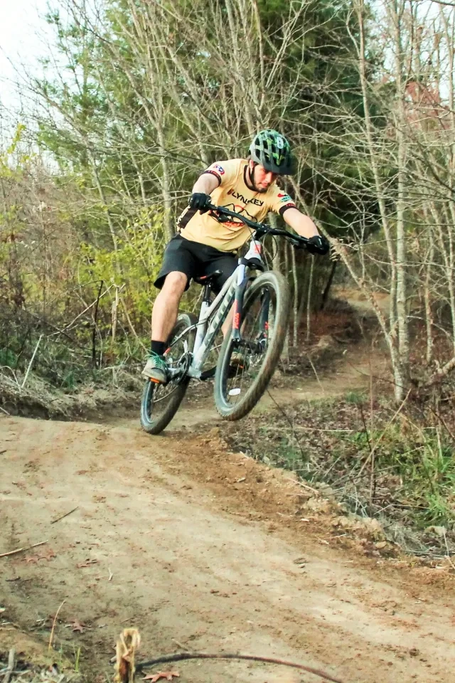 Cyclist jumping on a dirt trail in a wooded area.