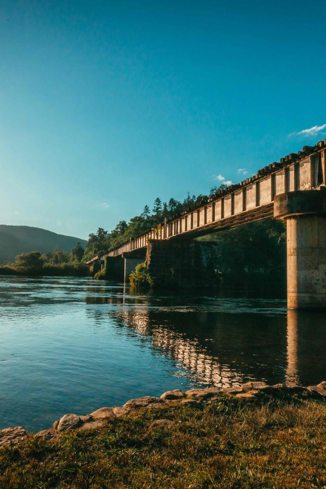 view of under a bridge during a sunset with water reflecting the sun and a mountain in the distance
