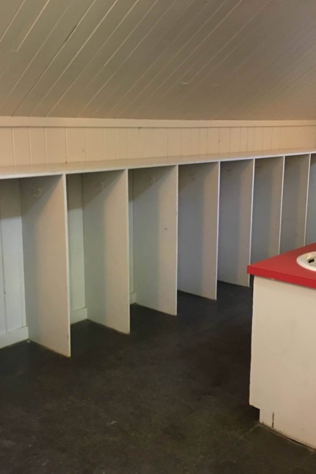 Angled view of a room with sloped ceiling, showing multiple white cubbies and hooks. A red countertop with a single sink is on the right.
