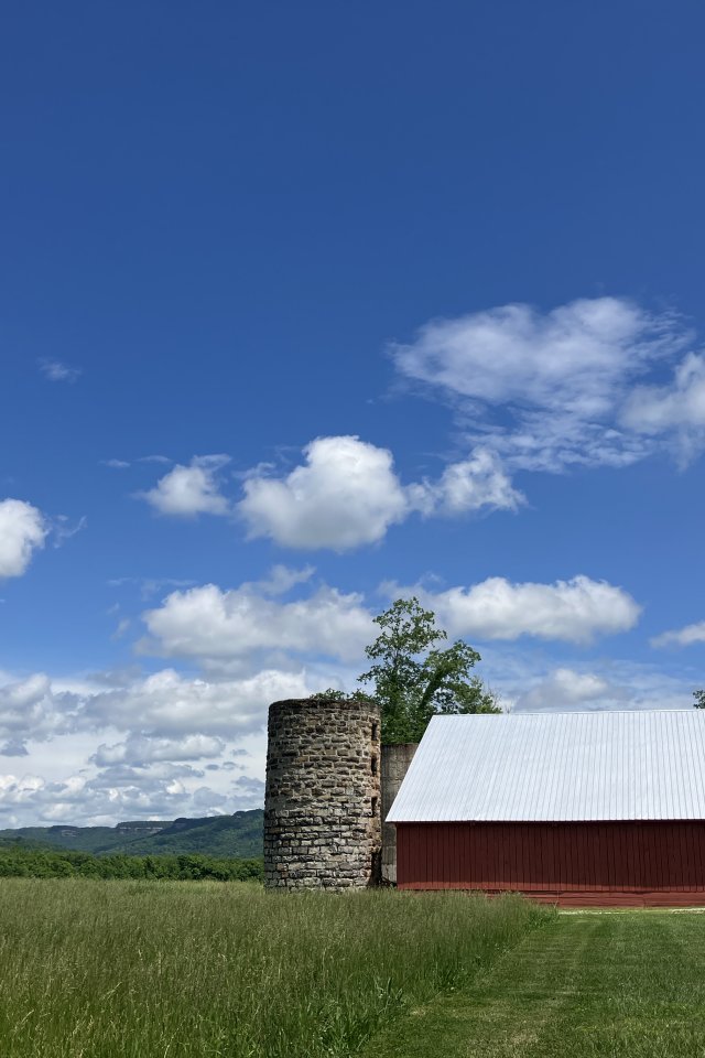 Red barn with silo under a blue sky with clouds.