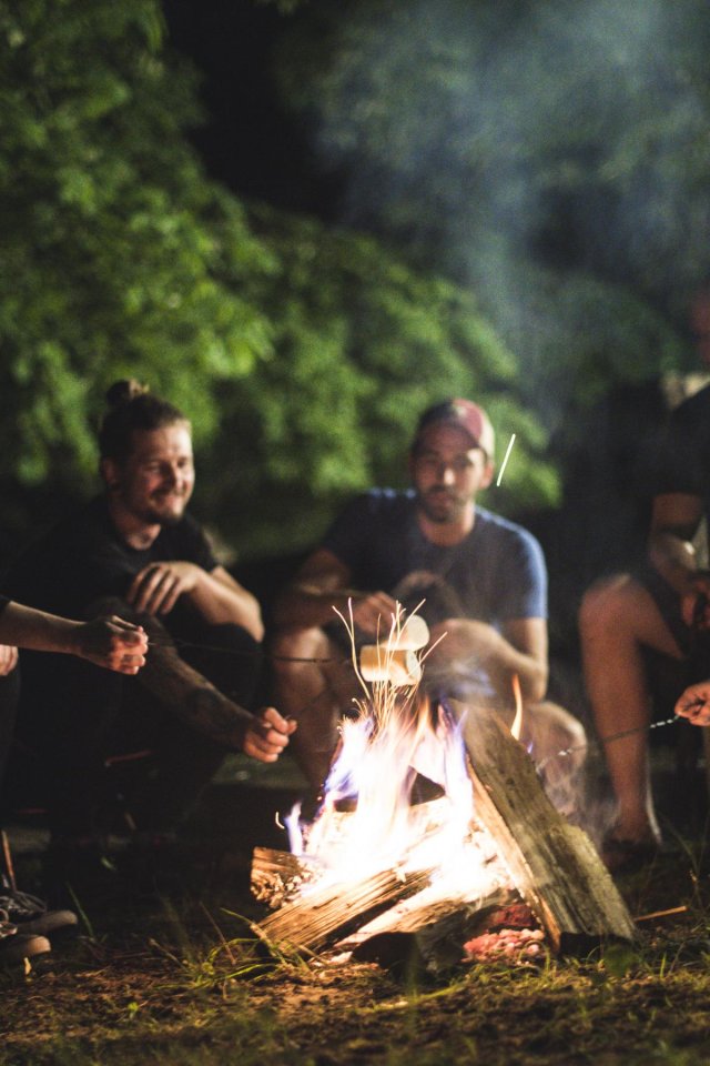 Group of people cooking marshmallows in the dark over a fire.