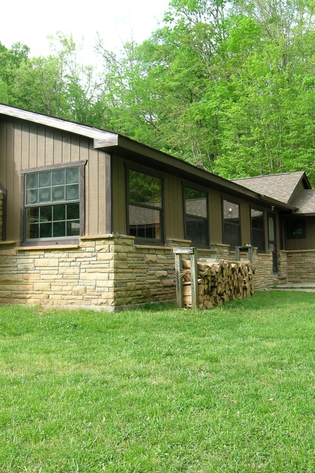 Cabin with stone chimney surrounded by lush green grass and trees.