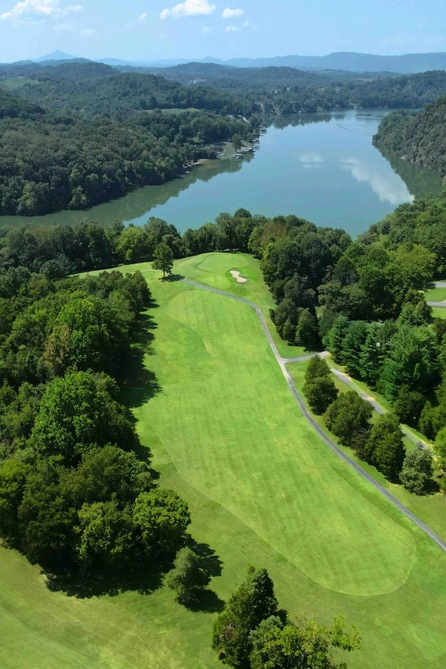 A vibrant green golf course lined with trees that leads up to a lake