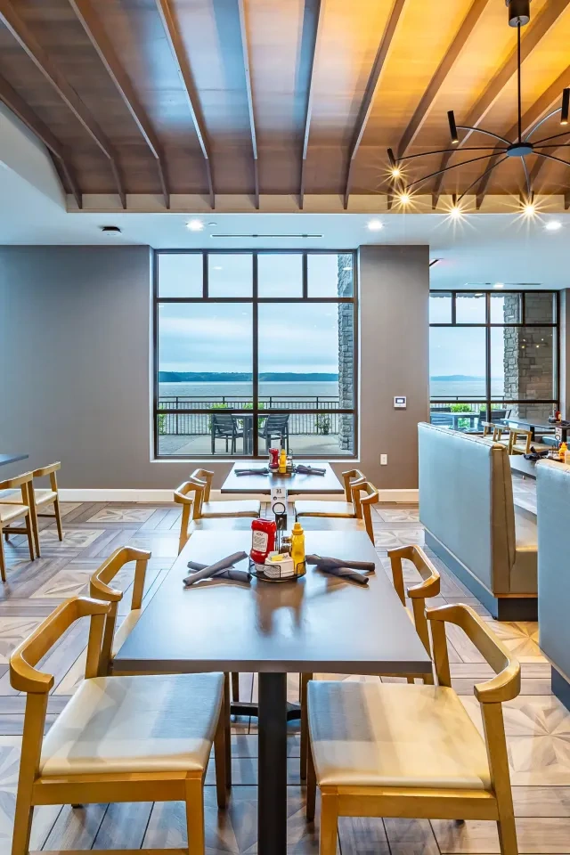 The interior of a restaurant with booths, tables and chairs looking out over a lake view