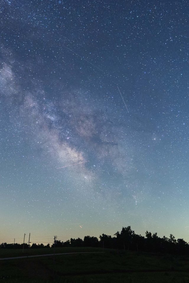starry night sky making a line in the sky with trees in the distance