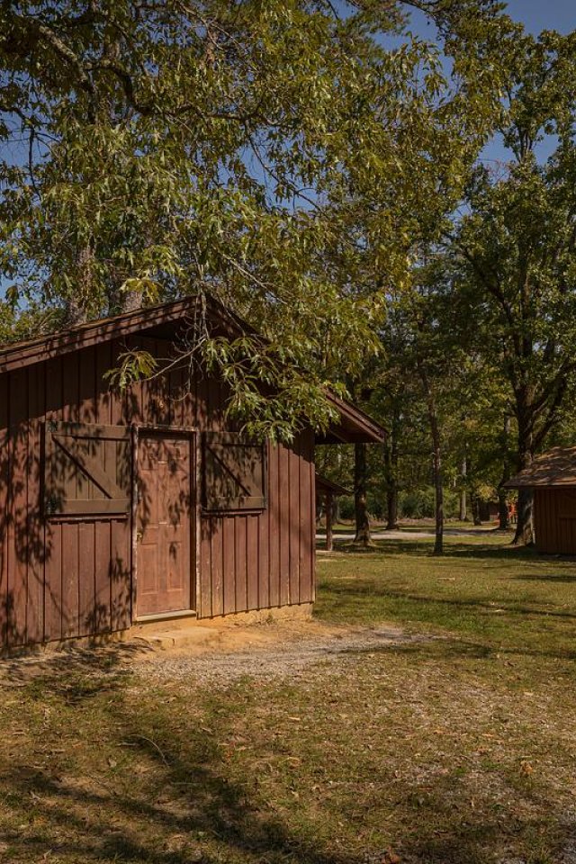 Brown wooden cabins in a forest clearing with sunlight filtering through trees.