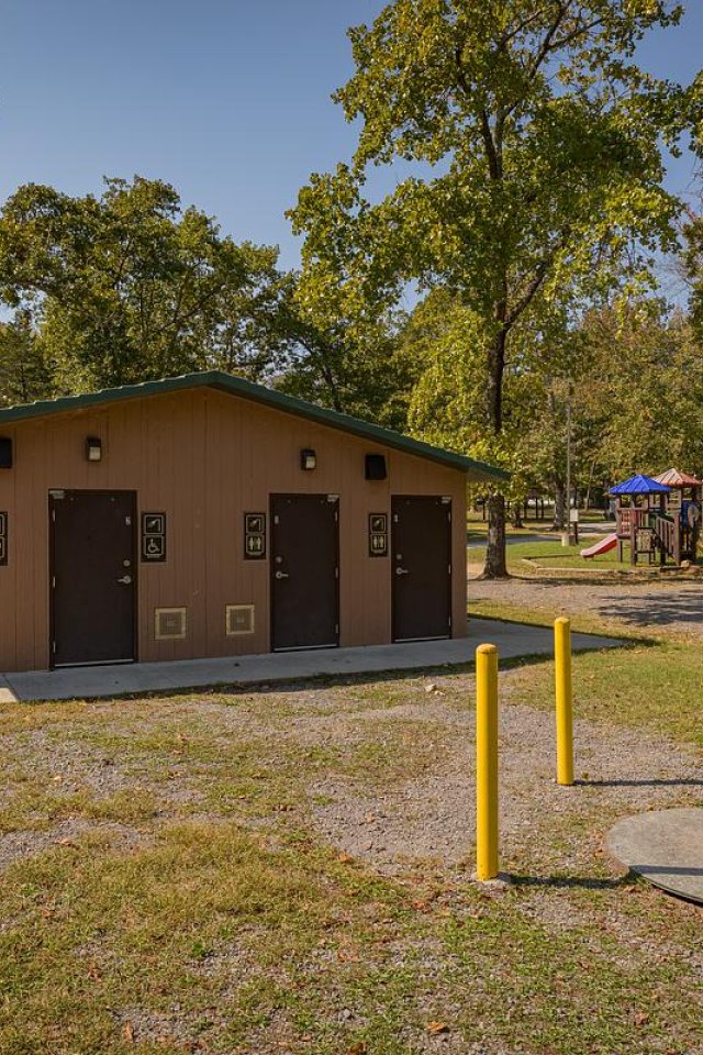 Restroom building in a park with trees and playground in the background.
