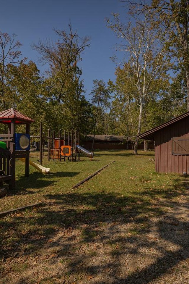 Playground with climbing structure, slide, and wooden shed on a sunny day.