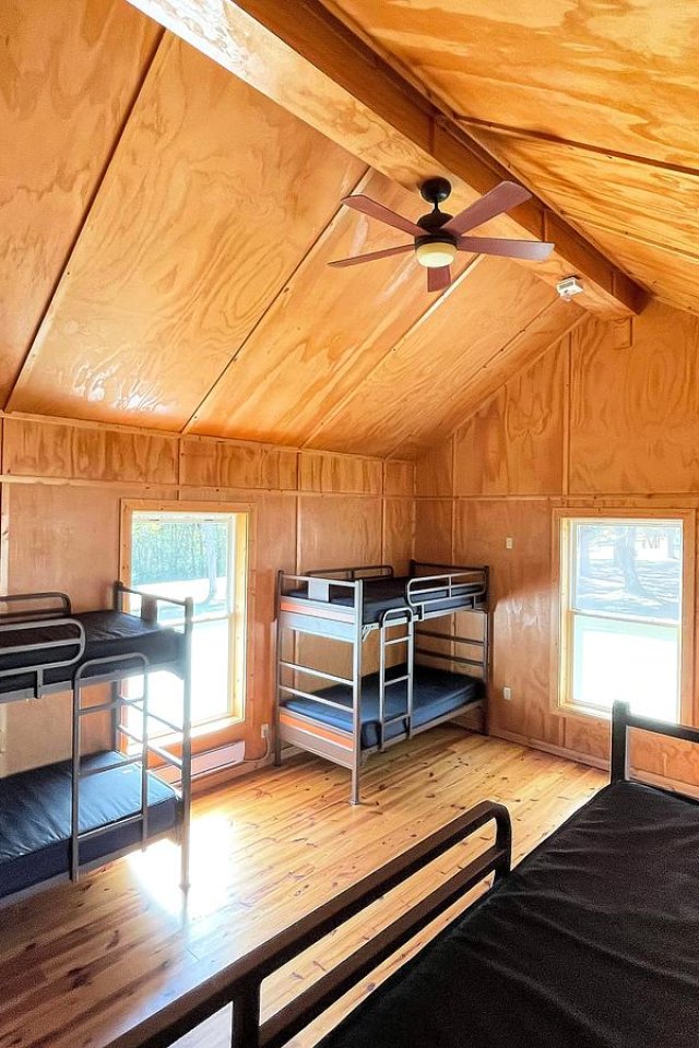 Interior of a cozy cabin with multiple wooden bunk beds and sunlit windows.