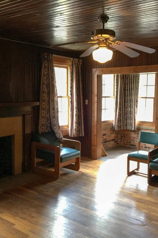 Cozy wooden living room with fireplace, chairs, and a ceiling fan.