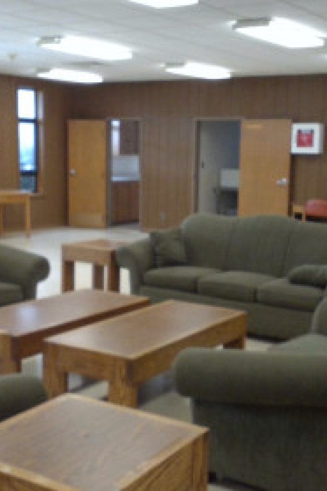 A spacious room with green couches and wooden tables.