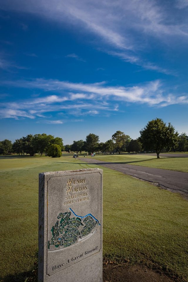 Golf course scene with blue sky, trees, and a course map sign in the foreground.