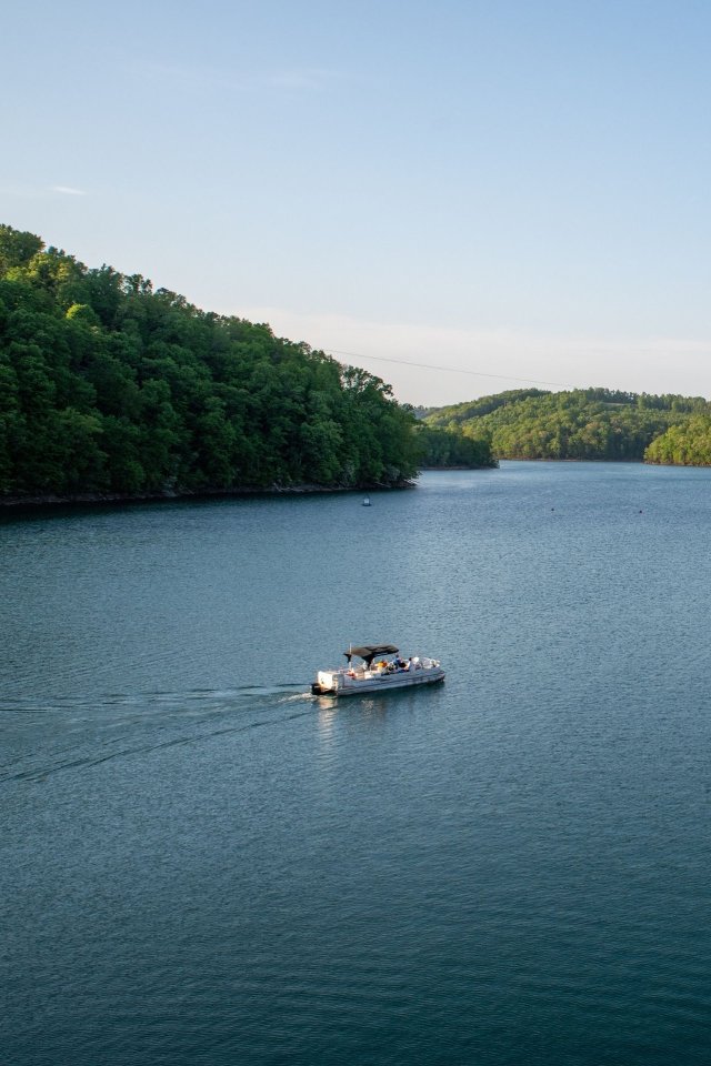 Boat cruising across a calm lake surrounded by forested hills.