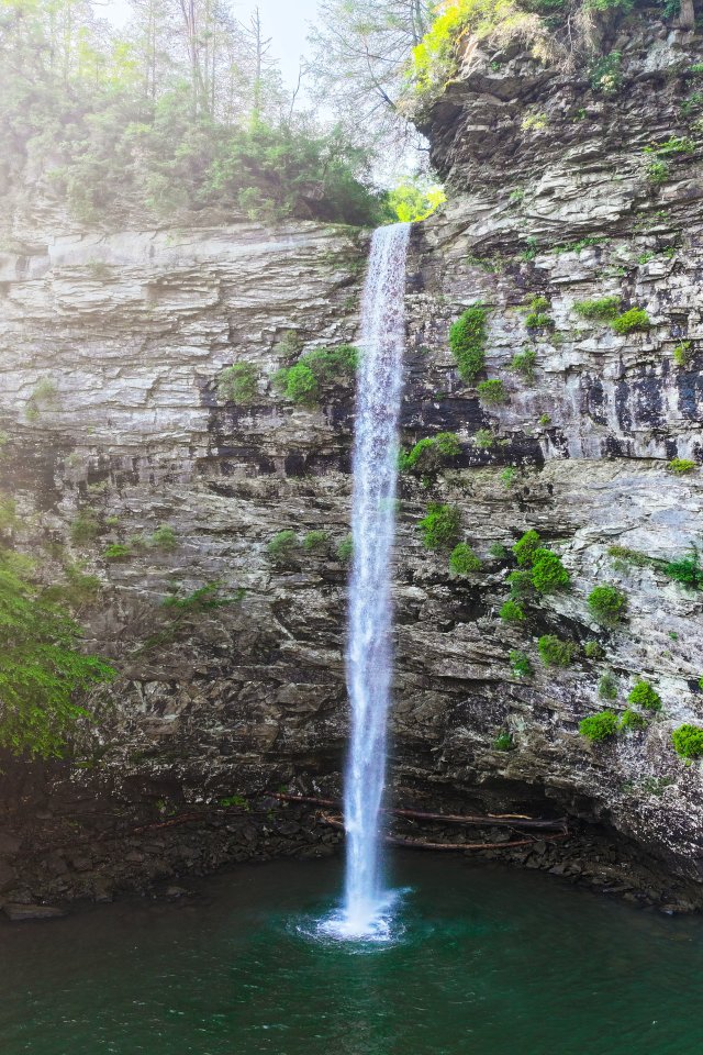 Tall waterfall cascading into a rocky pool surrounded by cliffs and trees.