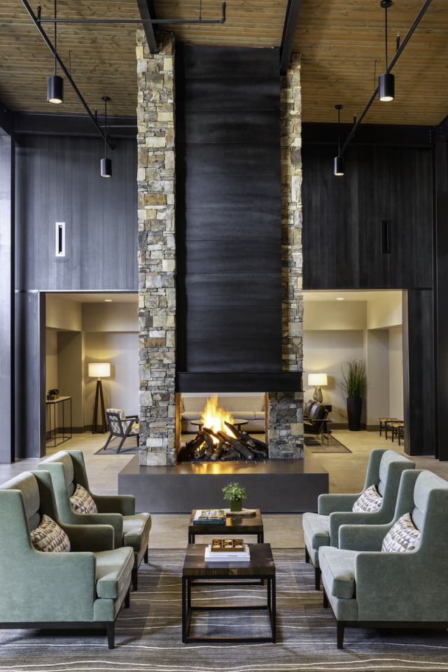Modern lobby with stone fireplace, green armchairs, and warm lighting.