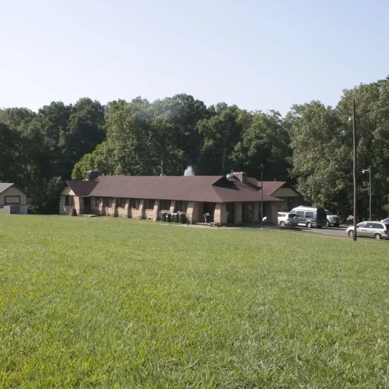 Lodge building with cars, surrounded by trees and grassy field.