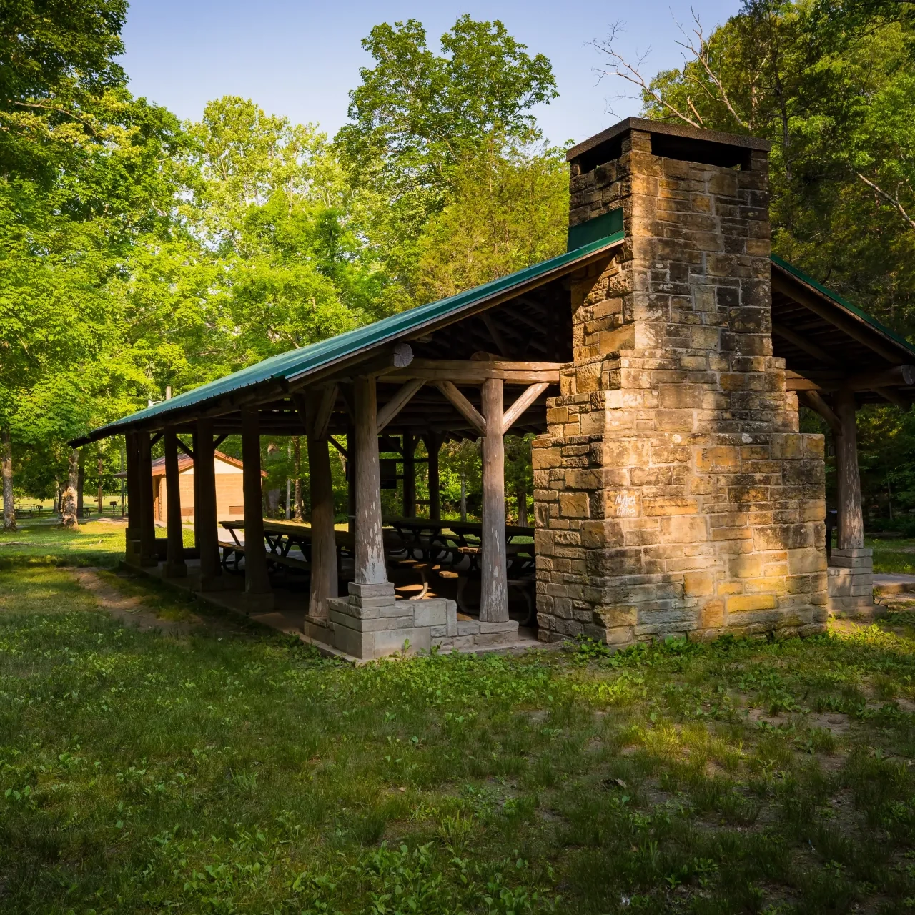 Stone picnic shelter with green roof, set amidst lush trees.