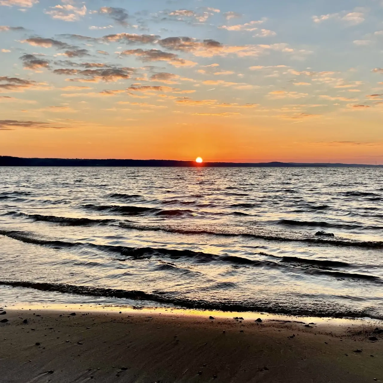 Sunset over the ocean with gentle waves and an orange sky.