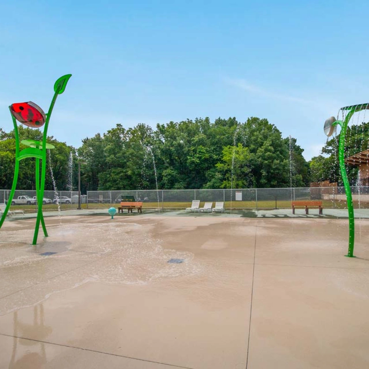 Children's splash pad with water fountains and ladybug sculpture.