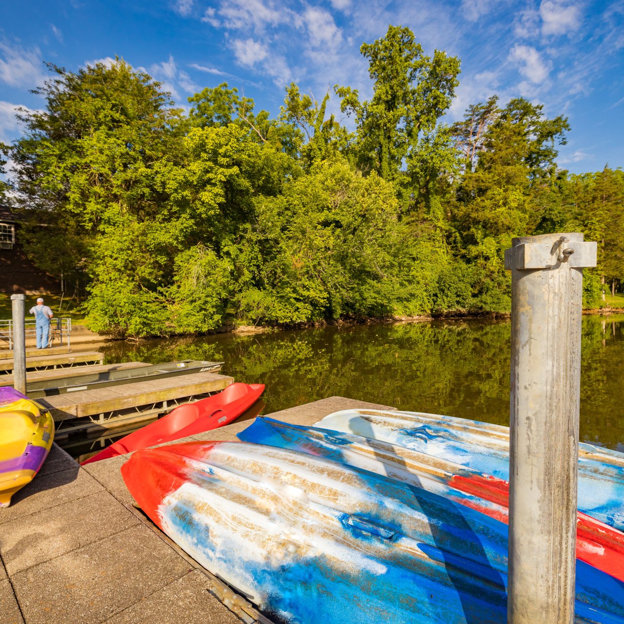 Dock with kayaks beside a calm lake surrounded by trees.