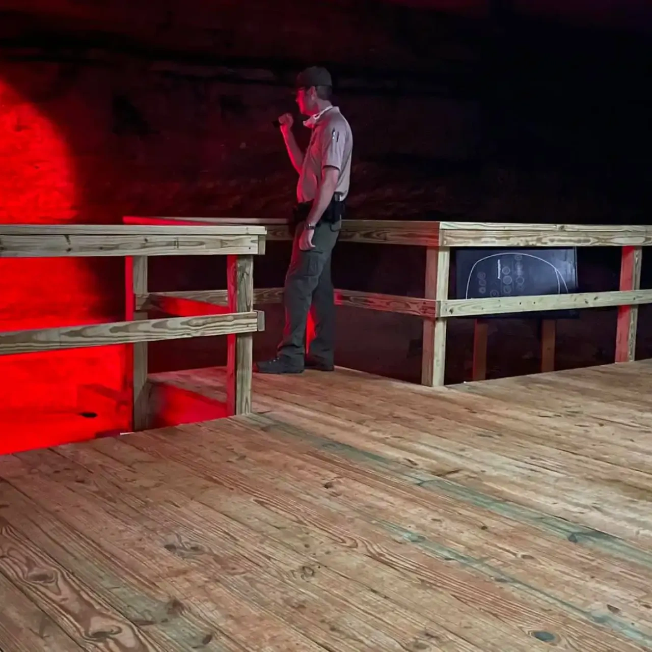 Man with flashlight on wooden platform, red-lit background.