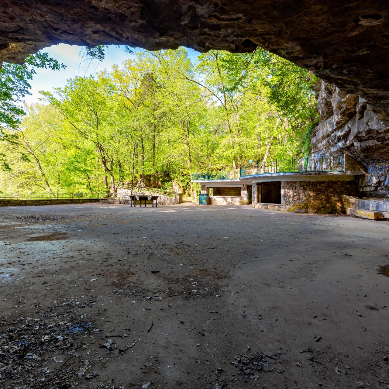 Cave foyer with rock walls, trees in the background, sunny day.