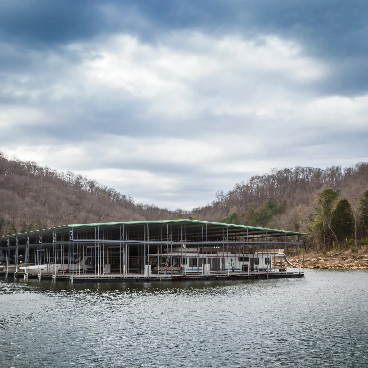 Floating dock on a lake, surrounded by wooded hills under a cloudy sky.