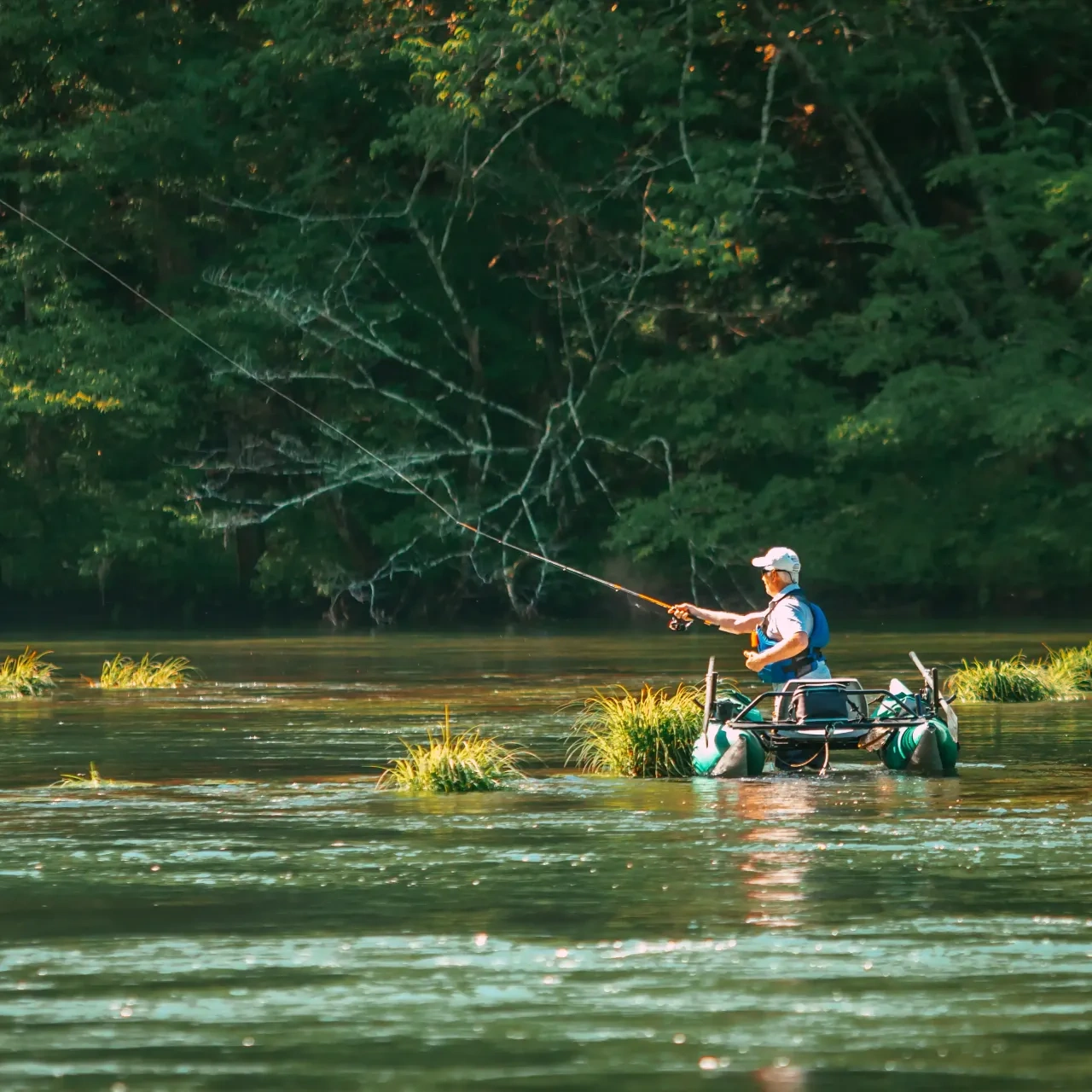 Man fishing in a river from a small inflatable boat, surrounded by lush greenery.