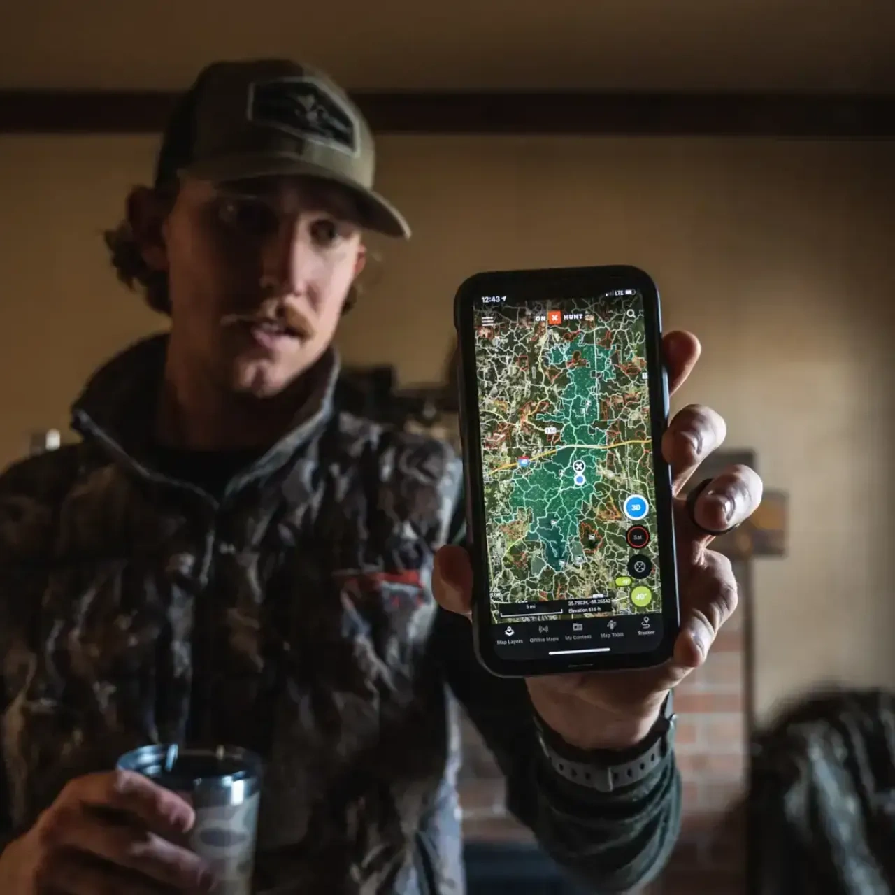 Man indoors holding smartphone with map app displayed.