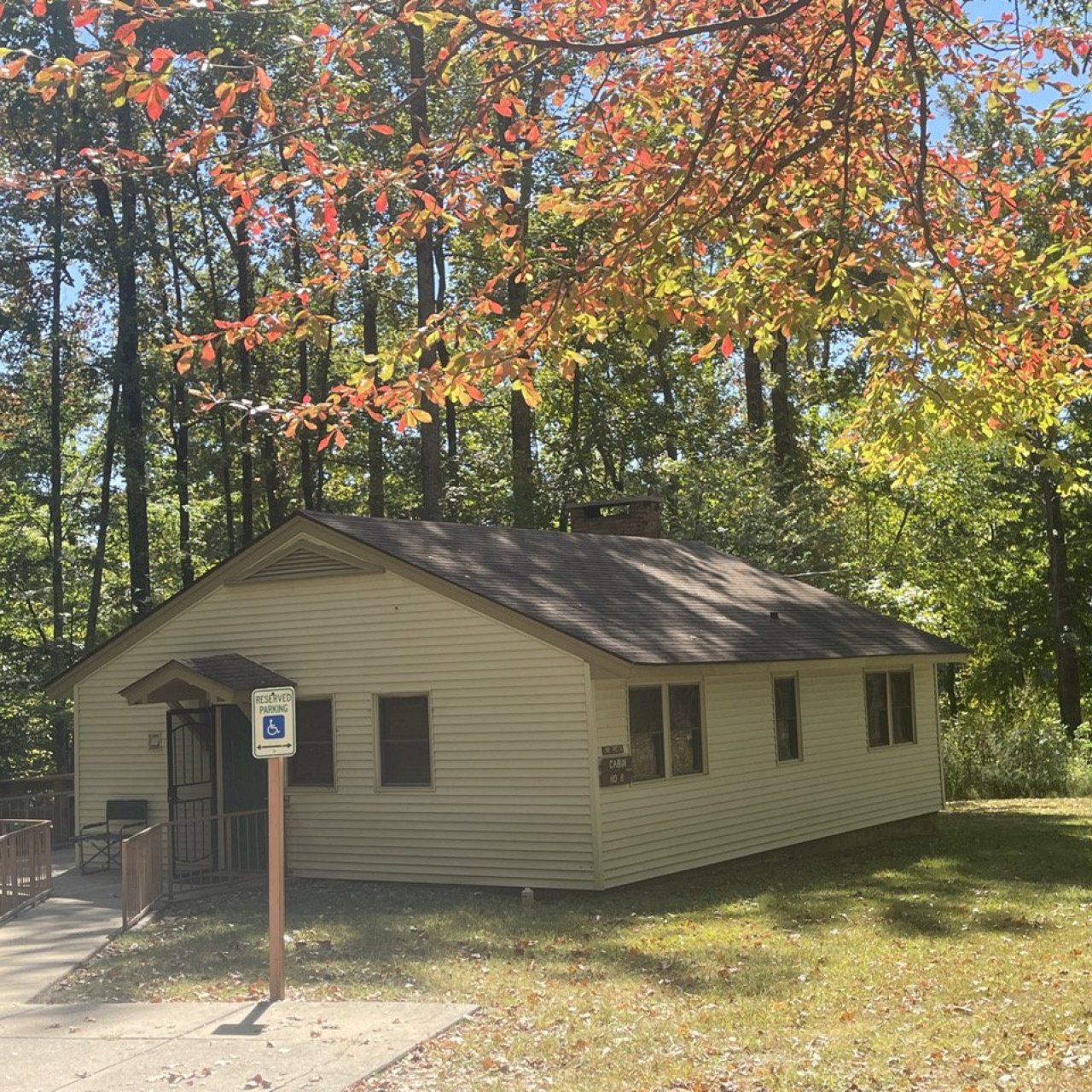 A small, beige cabin with a sloped roof. A ramp and handicap sign are visible in front.