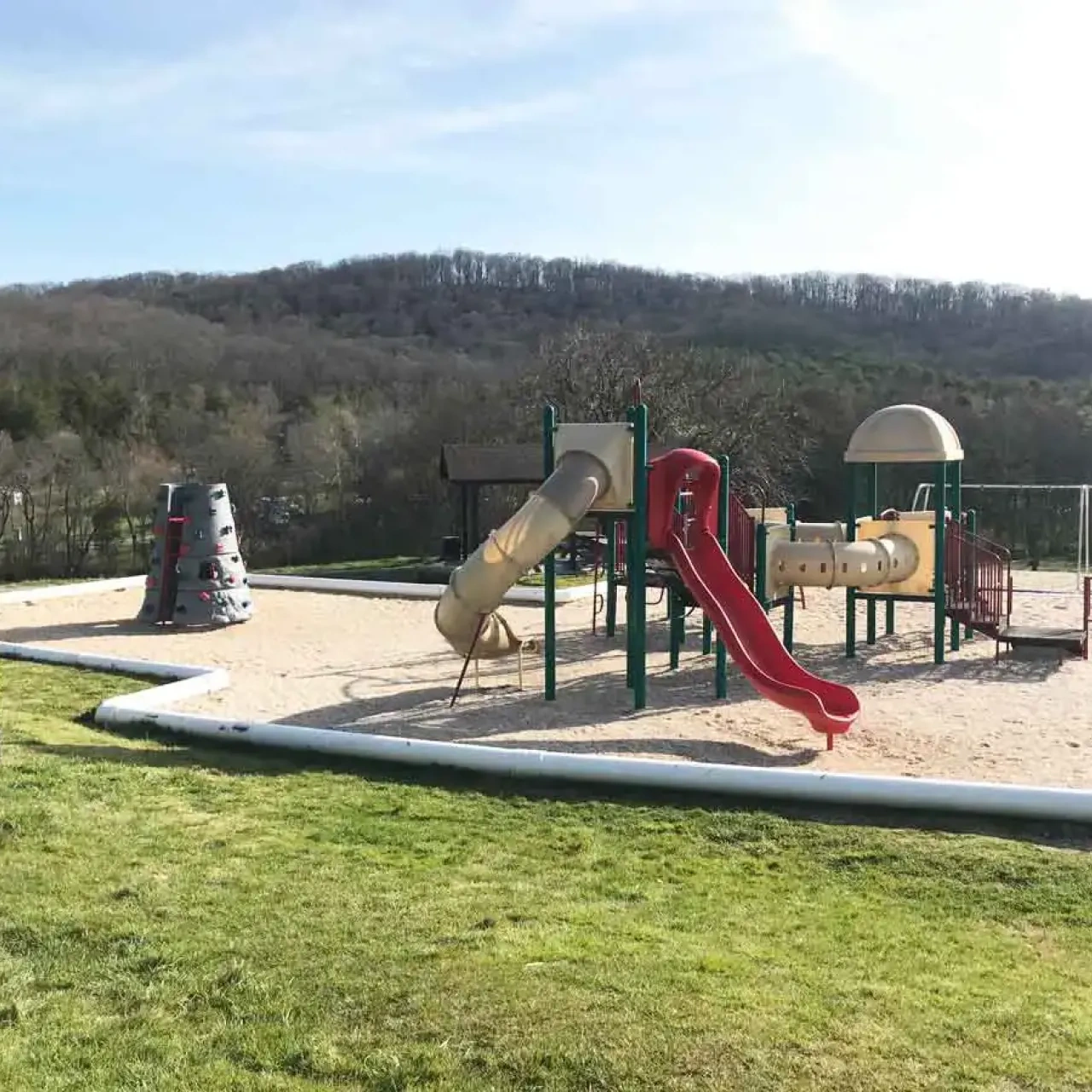 Playground with slides and climbing structures surrounded by scenic hills.