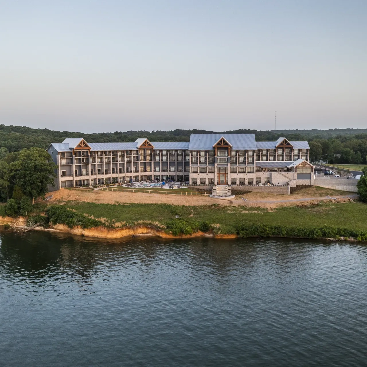 Lakeside hotel surrounded by trees at sunset.