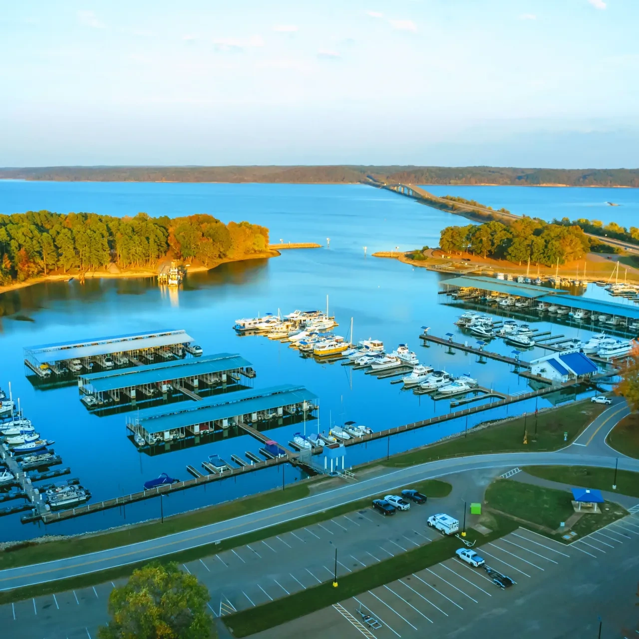 Marina with boats docked, surrounded by trees and a blue sky.