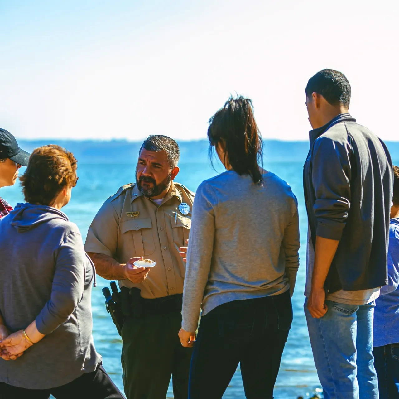 Officer speaking to a group by the water under a clear sky.