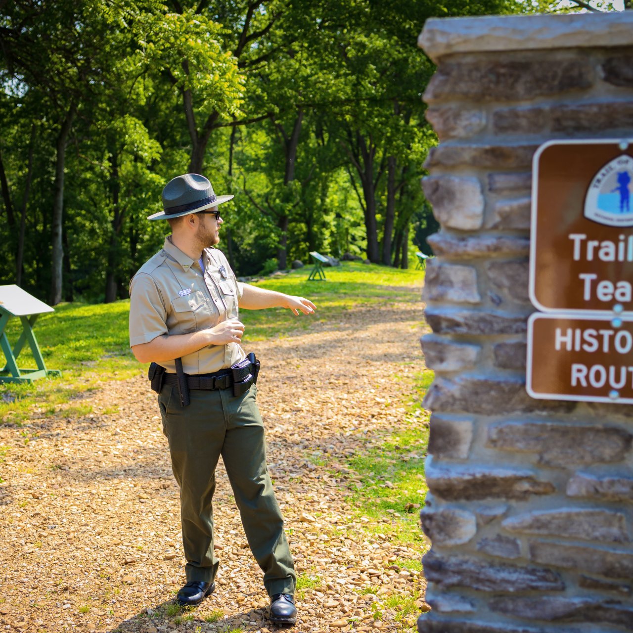 ranger standing on gravel trail of tears pointing. Brick post with "Trail of Tears" sign