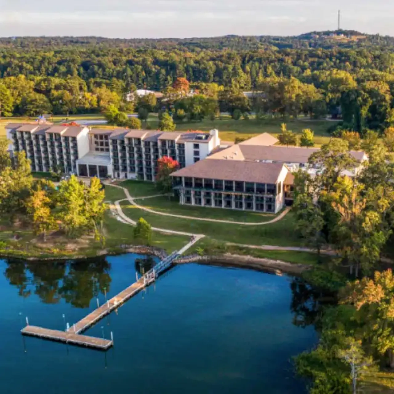 Large building by a lake, surrounded by trees and greenery.