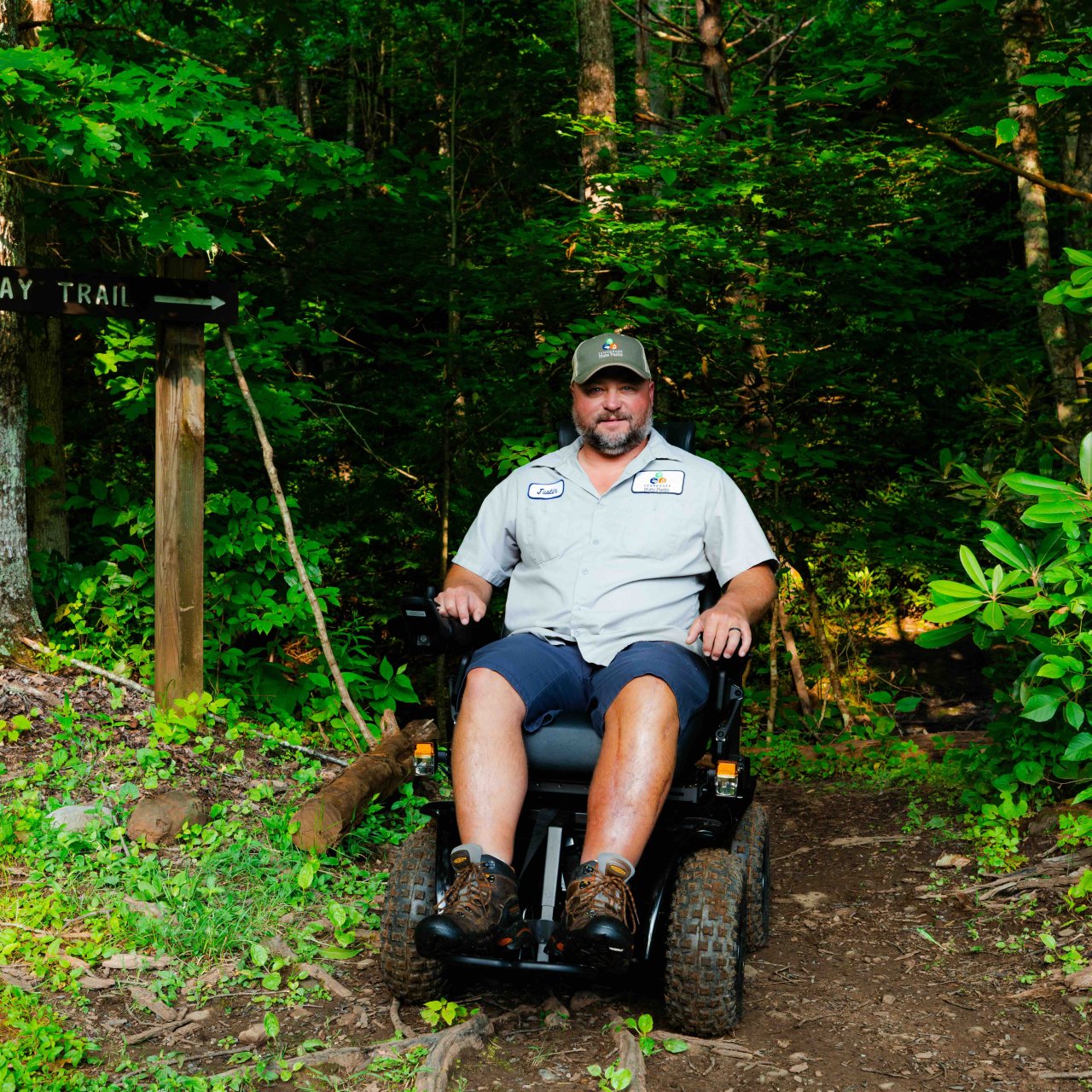 man sitting in all terrain wheel chair that is on a natural trail