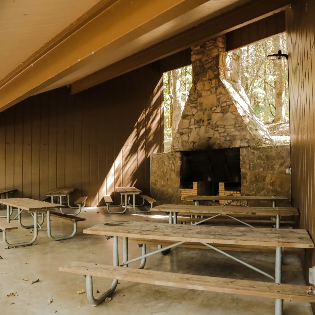 Covered picnic area with benches and a large stone fireplace.