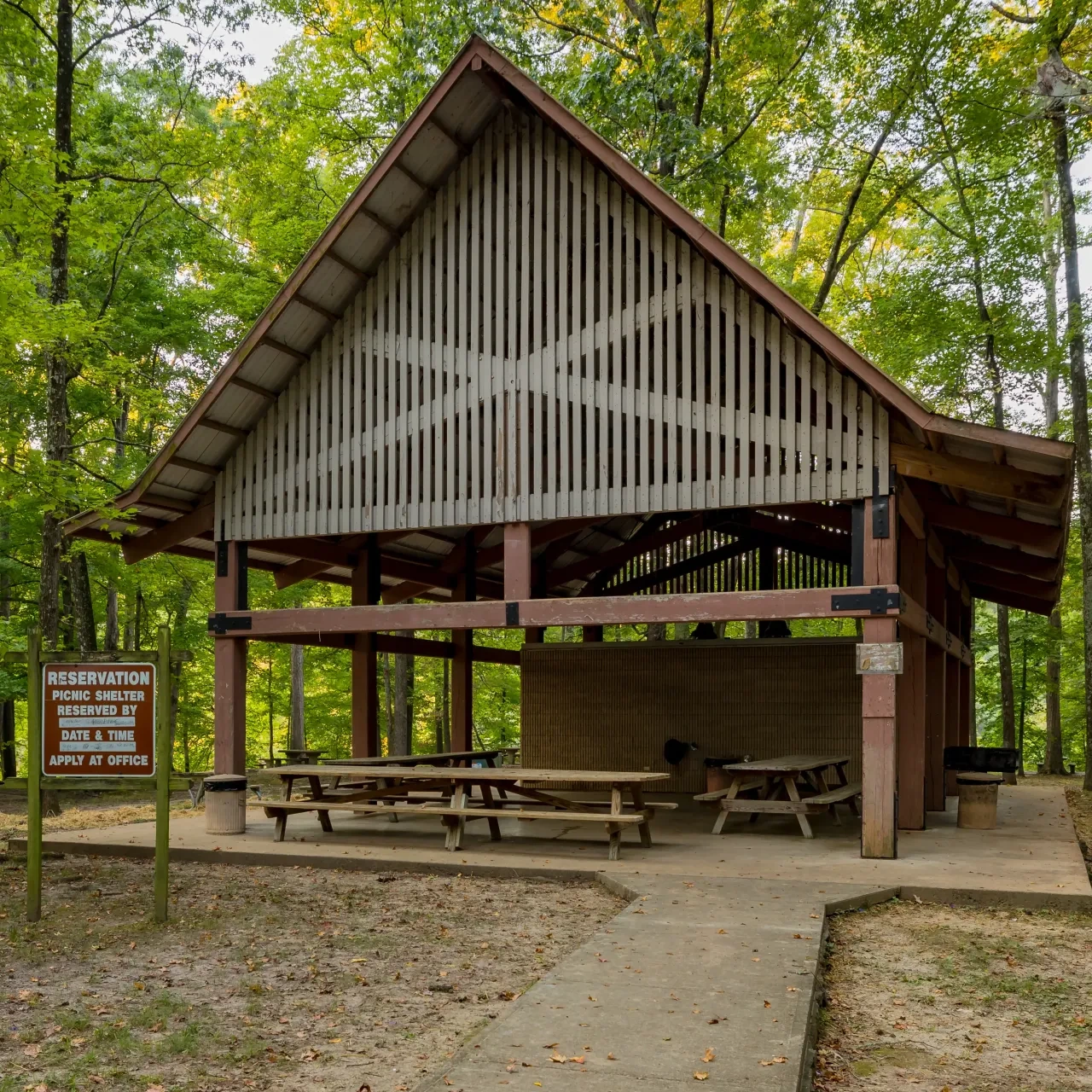 Wooden picnic shelter in a forest with tables and a reservation sign.