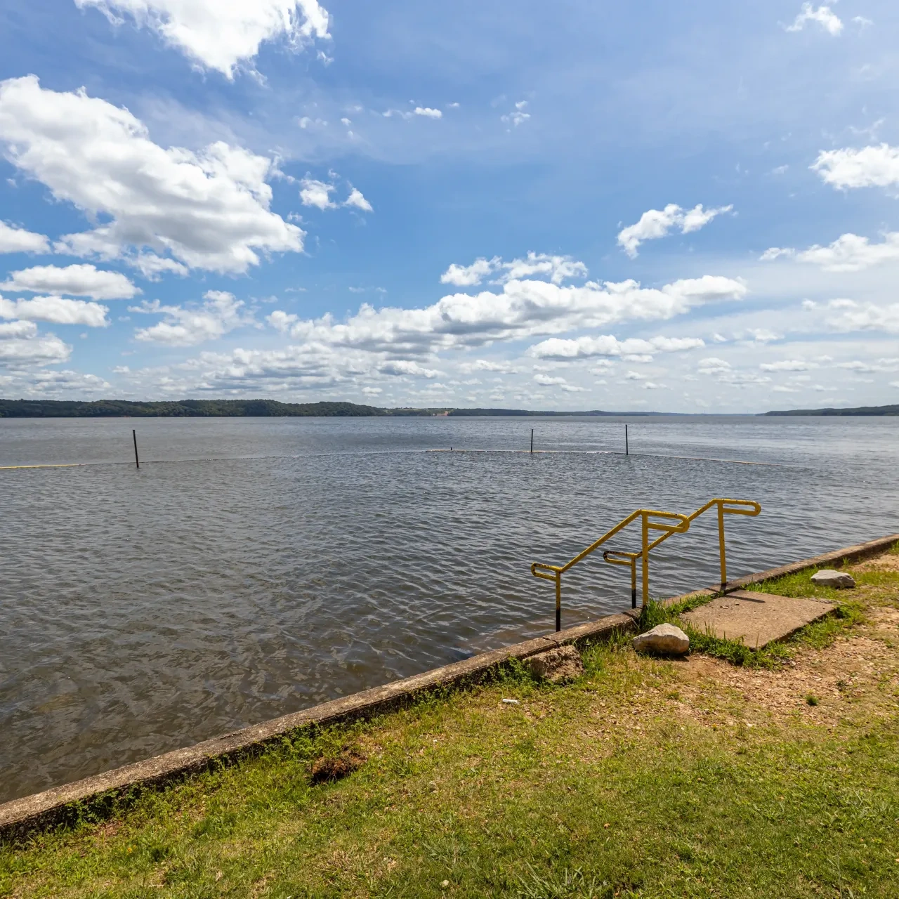 Lake with yellow railing, cloudy sky, and grassy shoreline.