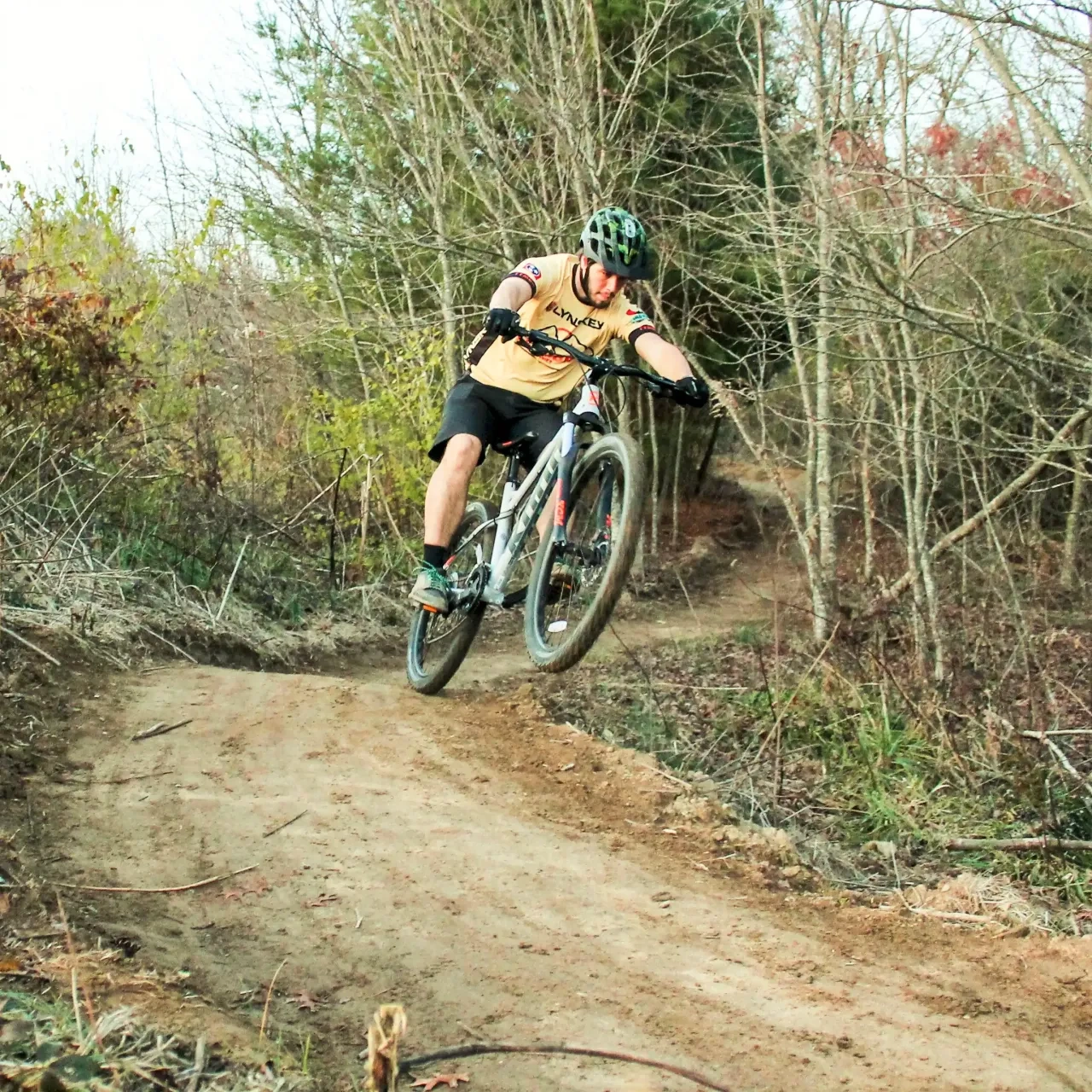 Cyclist jumping on a dirt trail in a wooded area.