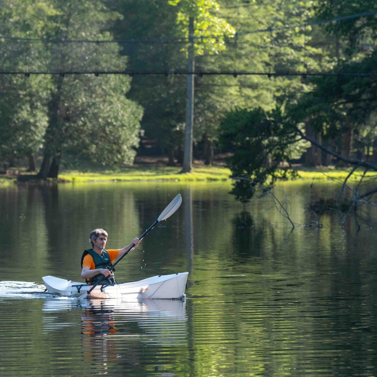 man paddling in a boat on calm water with a bridge above him