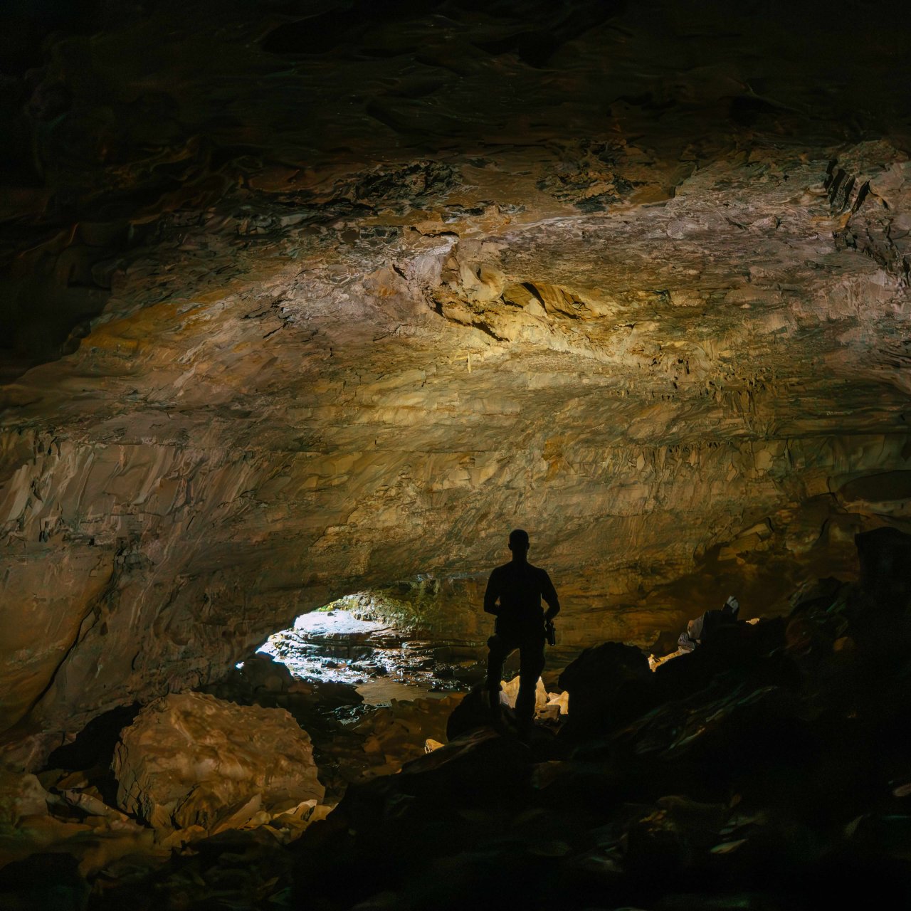 silhouette of a person standing in a cave with a light shining the top of the cave