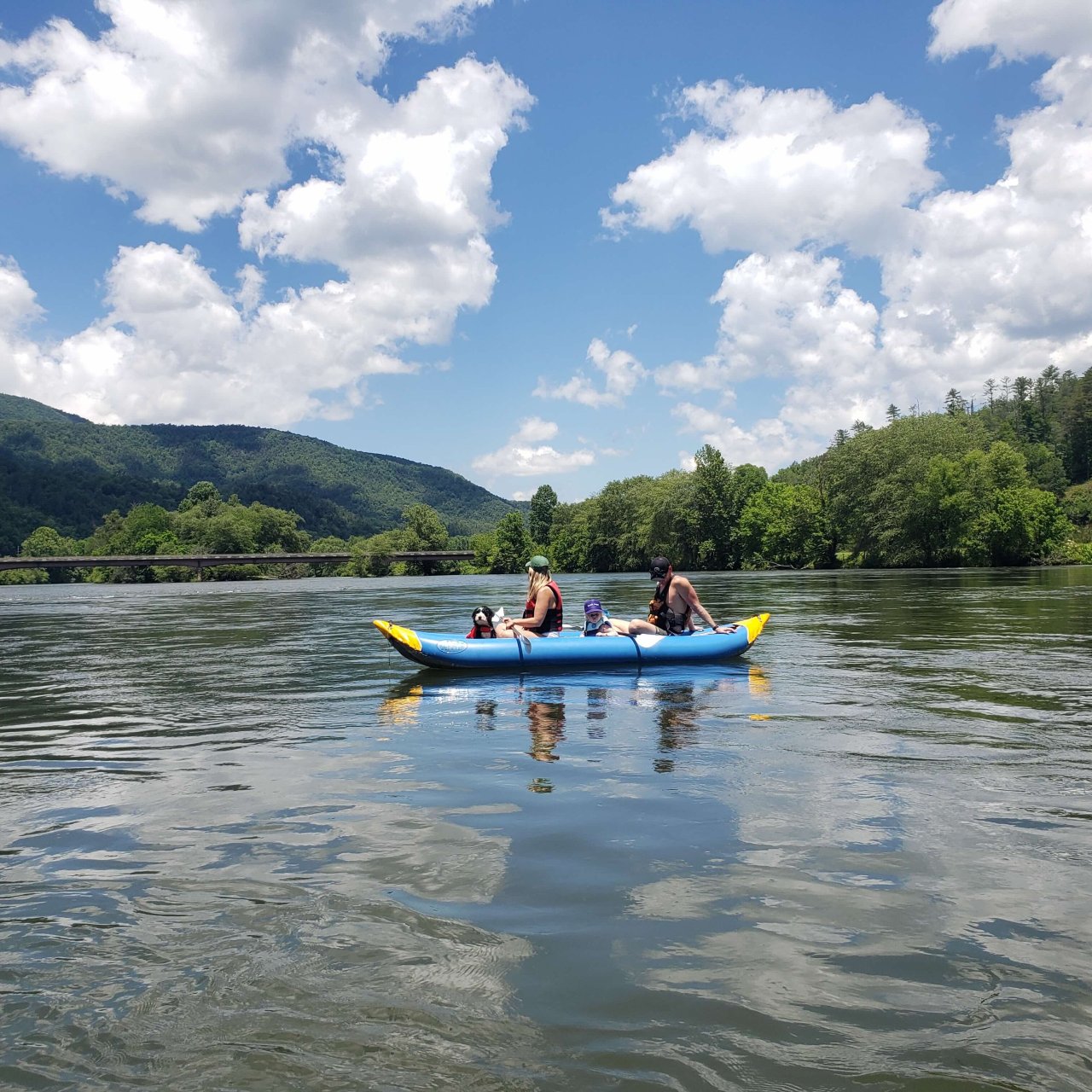 two grown women, a little girl, and a dog in a kayak paddling in lake with a view of mountain in the distance