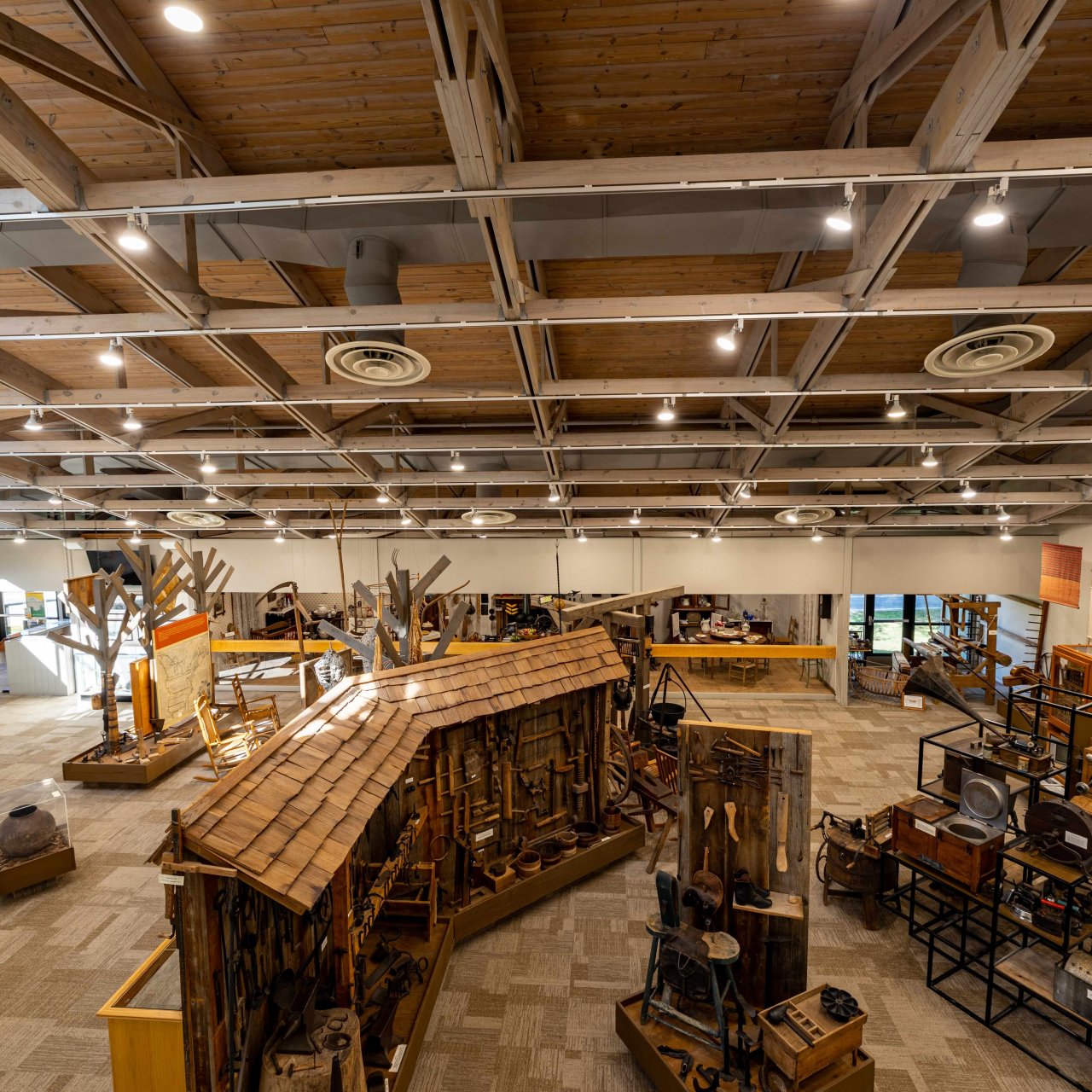 Spacious museum interior with rustic wooden exhibits, vintage tools, and machinery. High wooden ceiling and soft lighting create a warm, inviting atmosphere.
